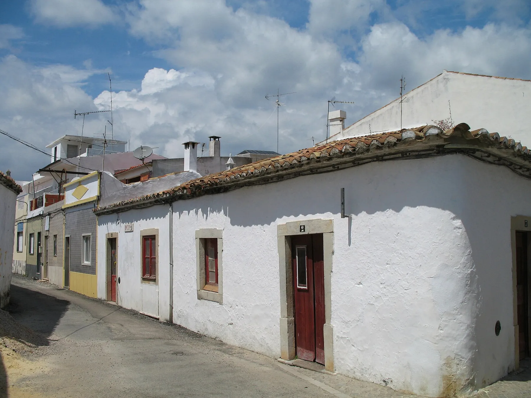 Casa térrea de esquina caiada de branco, com portas vermelhas e cantarias, numa rua de São Brás de Alportel
